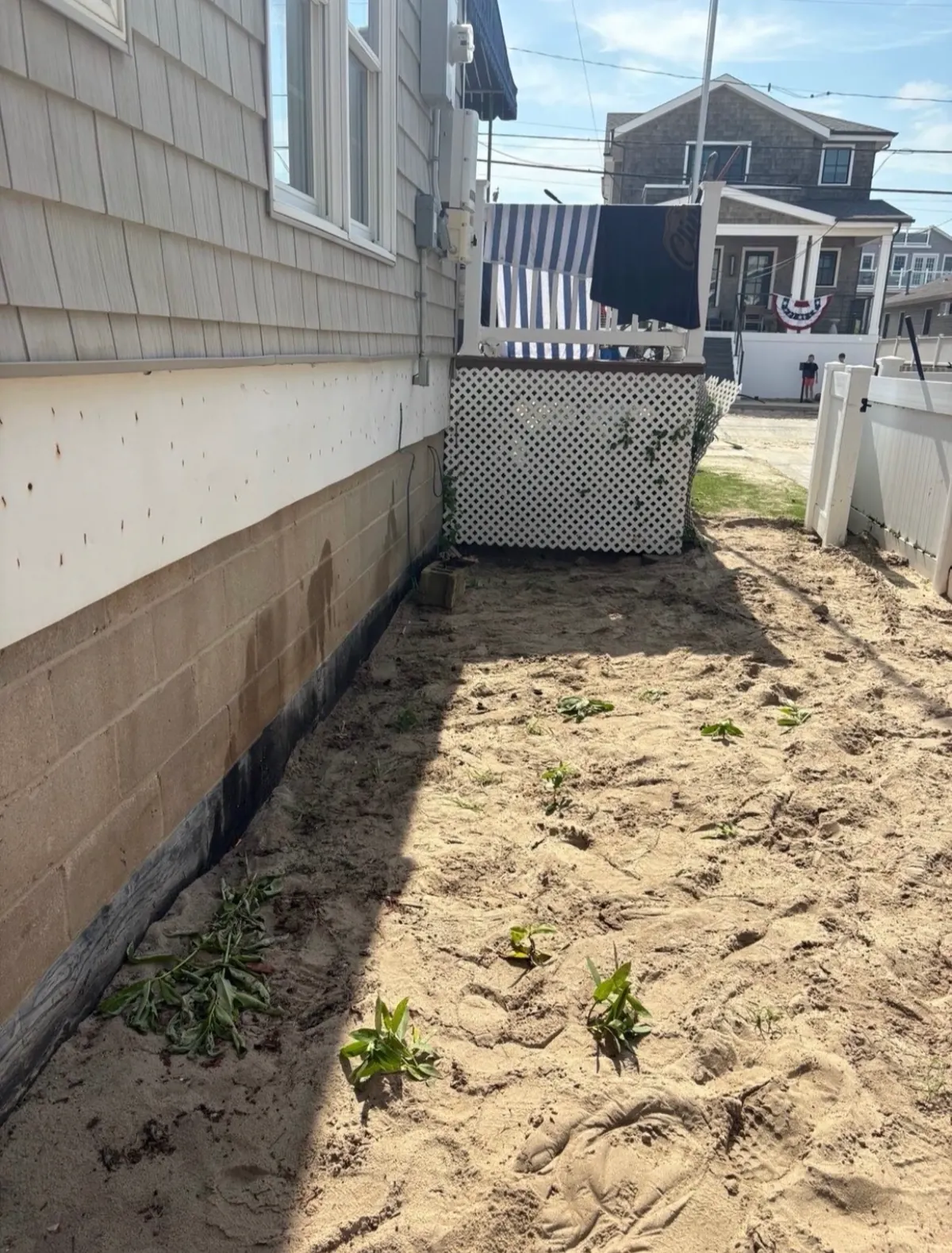 Side yard after: everything hauled away, leaving clear sand along the house