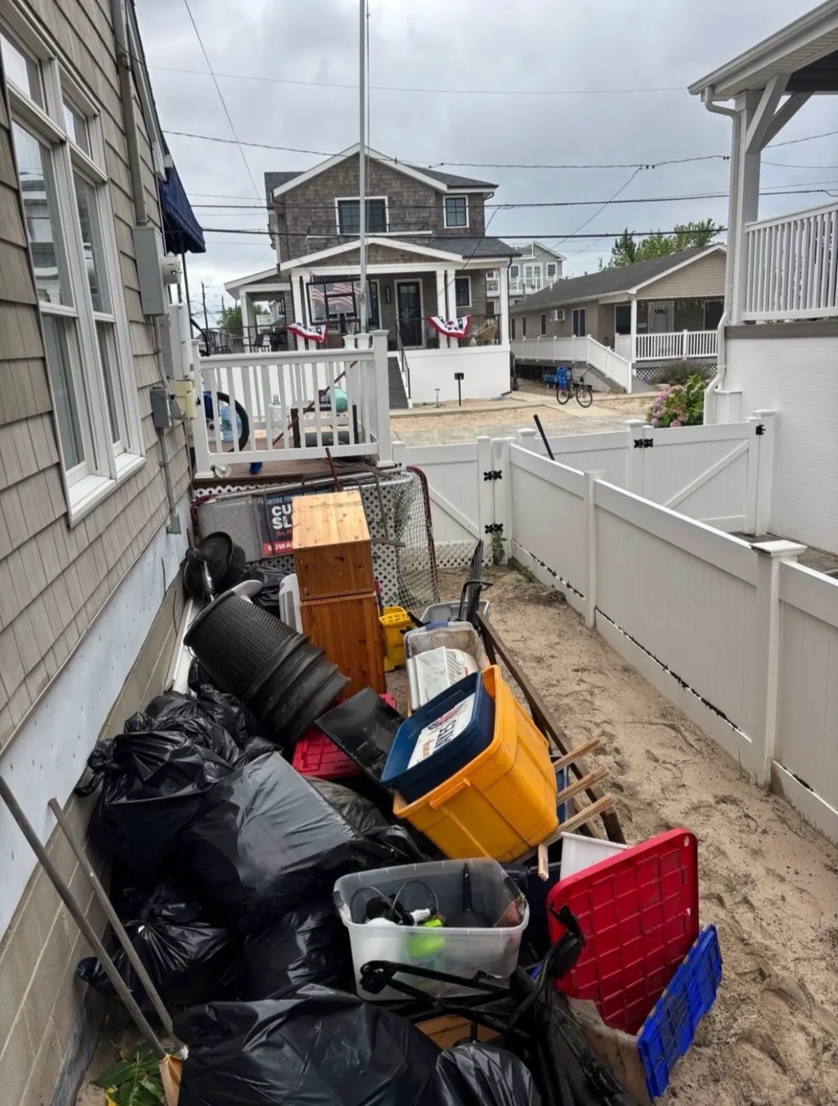 Side yard before: trash bags, bins, a cabinet and debris piled along the house